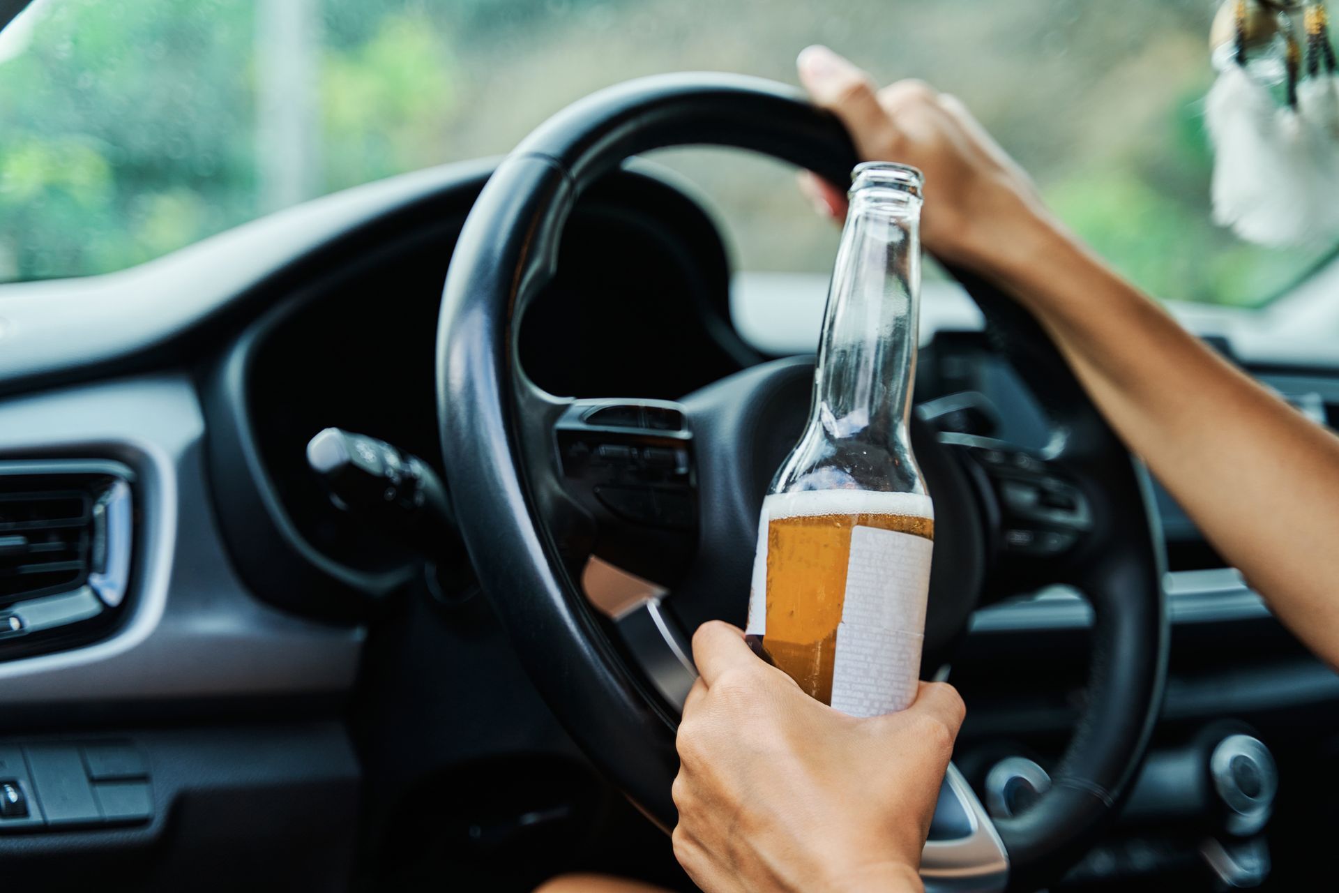 A person is holding a bottle of beer while driving a car.