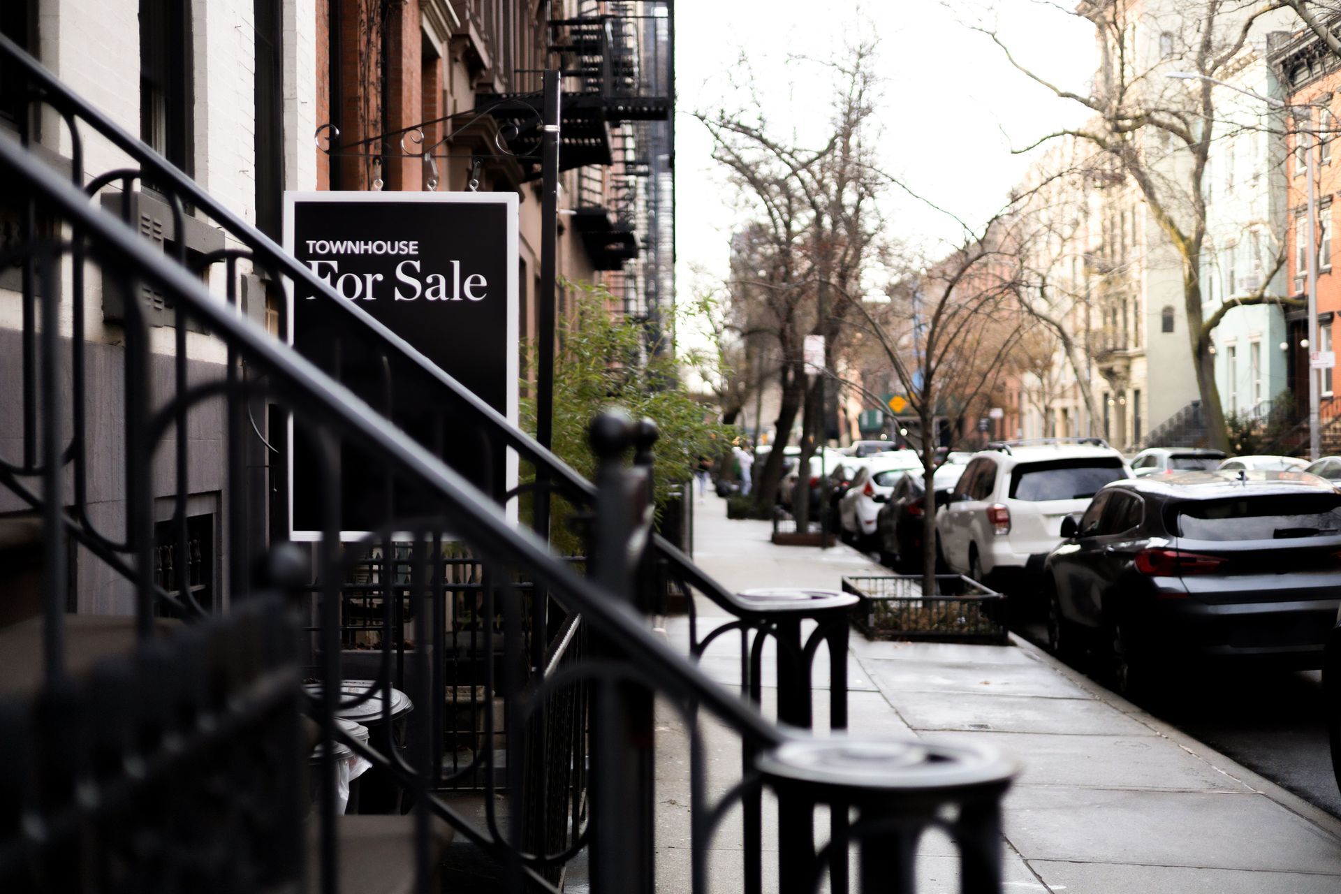 A for sale sign is on the sidewalk in front of a building.