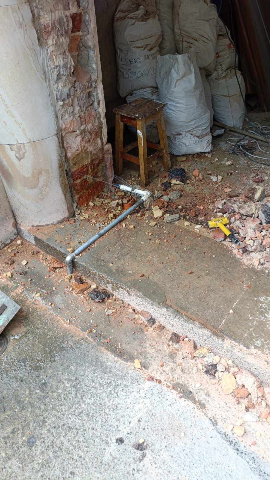 Entrada parcialmente demolida con escombros, ladrillos a la vista y un pequeño taburete dentro de una habitación dañada.