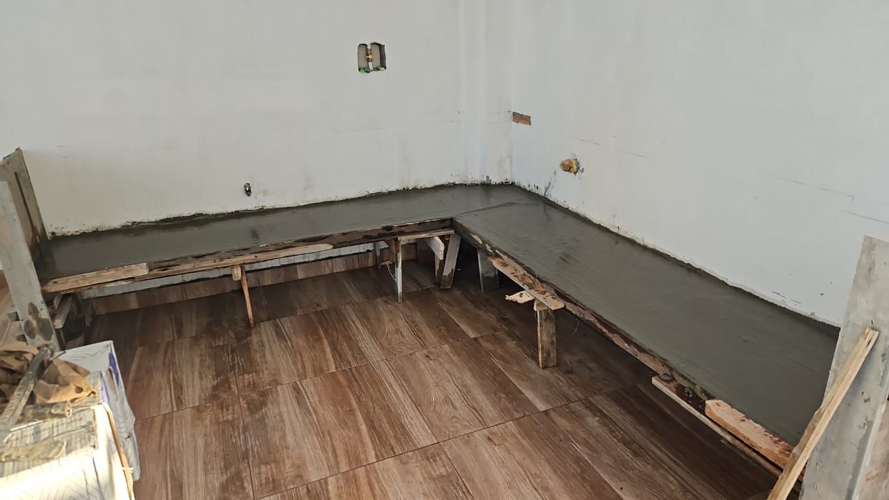 Cocina parcialmente demolida con la estructura del suelo a la vista y una encimera gris junto a paredes blancas.