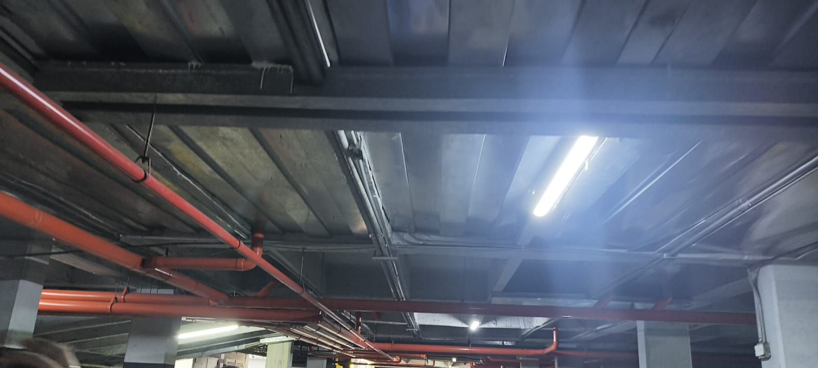 Techo industrial con tuberías a la vista y luces fluorescentes brillantes en el interior de un almacén.