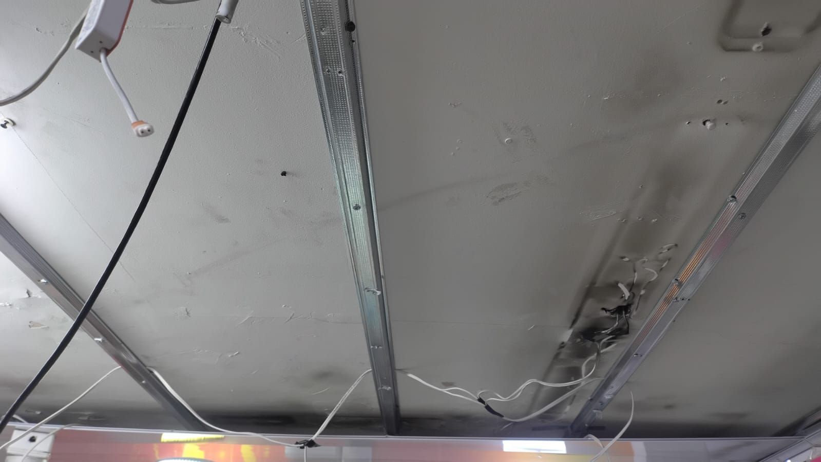 Techo dañado con paneles colgantes, cableado expuesto y vigas metálicas en un espacio interior.