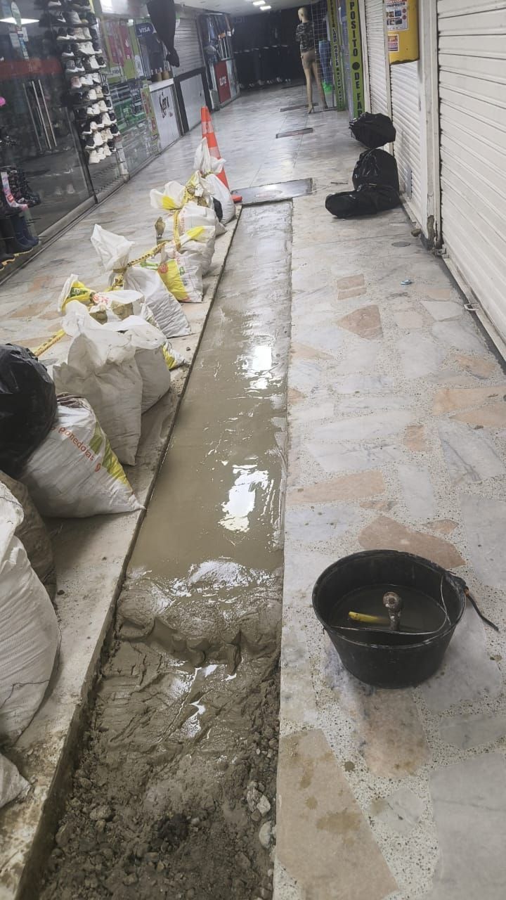 Un estrecho pasillo de entrada a una tienda está en reparación, con hormigón fresco, sacos de arena