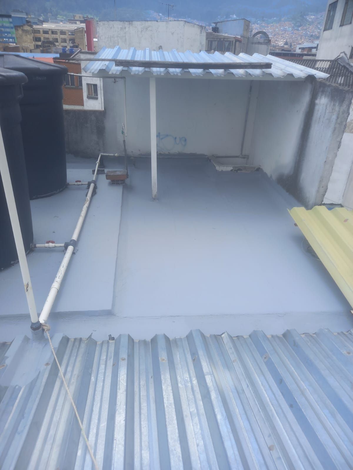 Terraza en la azotea con suelo gris, borde de techo de chapa ondulada y una pequeña zona de almacenamiento cubierta.