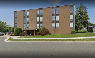 Brick building with multiple windows. Lawn and sidewalk in front. Trees and overcast sky in background.