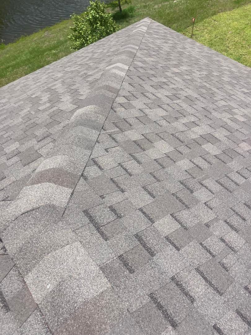 Gray shingled roof with a ridge peak, bordered by green grass and trees