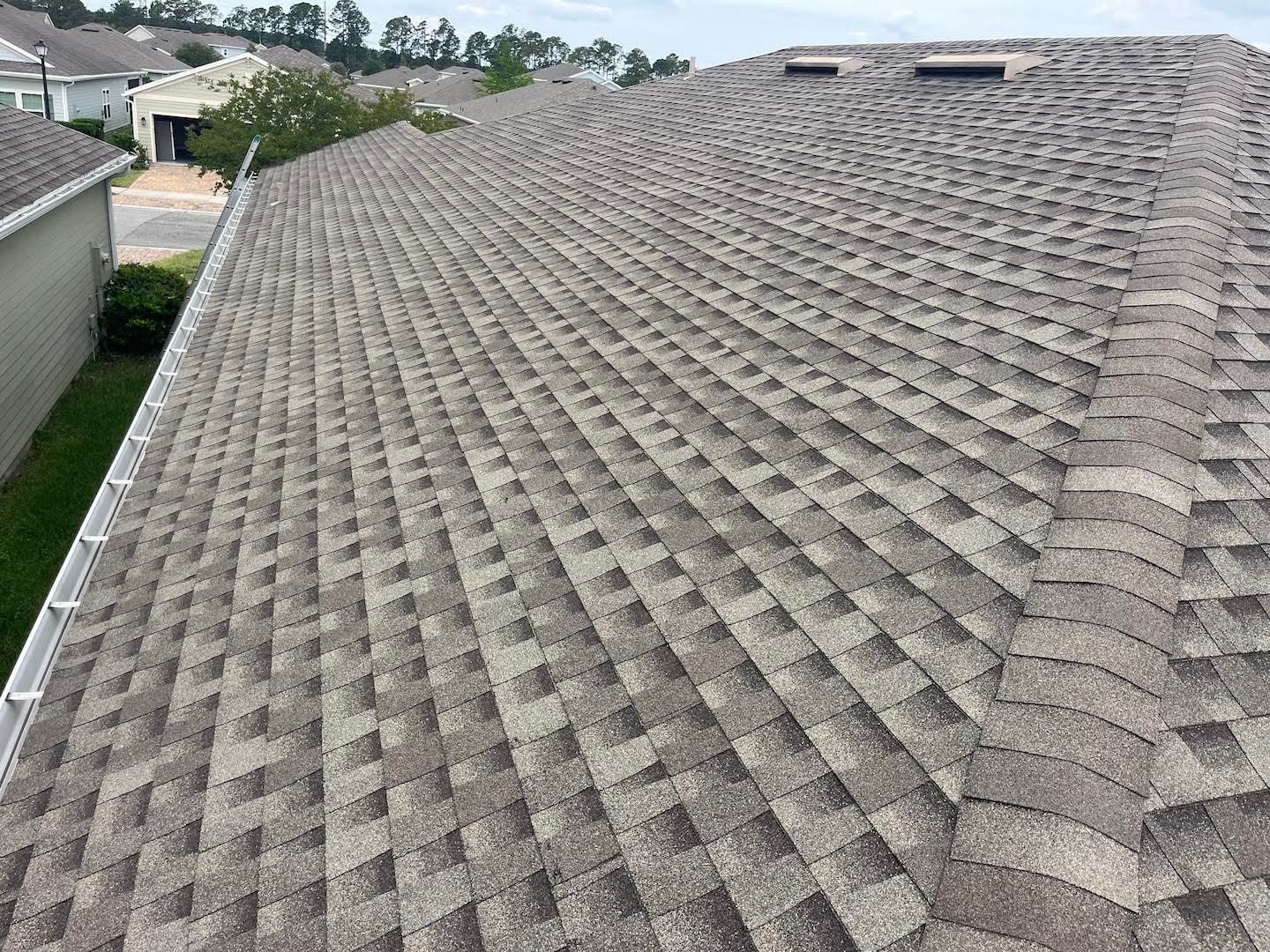 Close-up of a gray shingle roof on a house, with neighboring homes in the background.