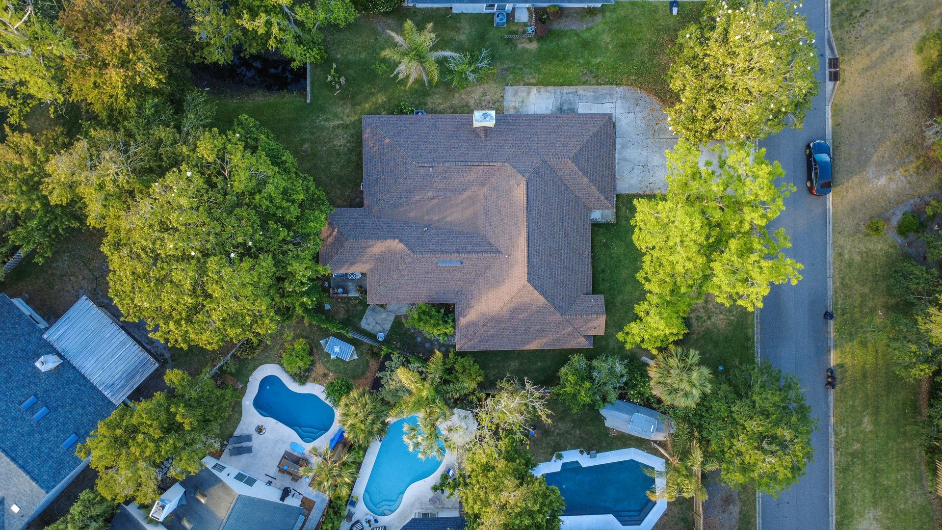 Aerial view of a house with a yard, trees, and three backyard swimming pools.