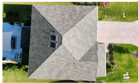 Aerial view of a gray-roofed house with a driveway, lawn, and neighboring homes.