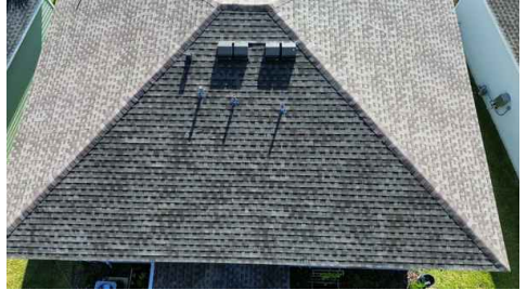 Aerial view of a steep shingled roof with two skylights and solar panels on the upper side.