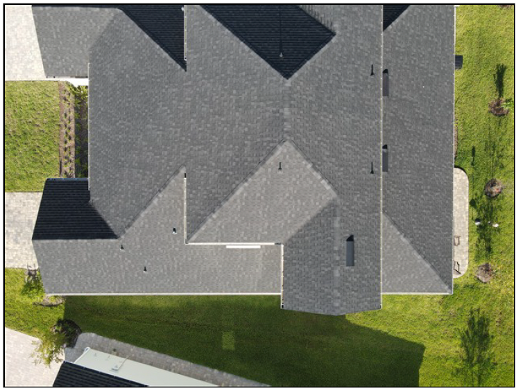 Top-down aerial view of a gray house roof with green lawn and driveway around it