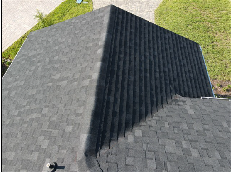 Roof with gray shingles and a dark, steep gable section in a grassy yard.