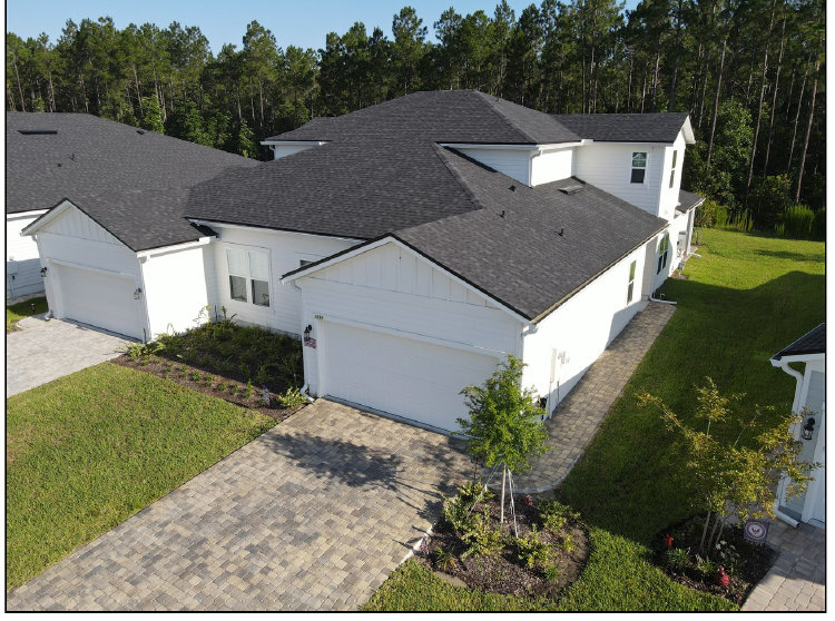 White suburban house with dark roof, driveway, and trees behind it
