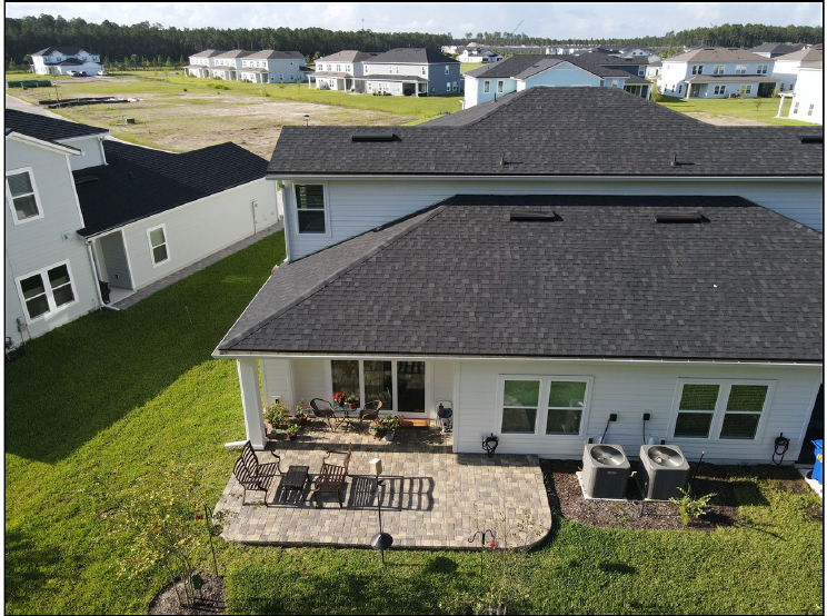 Aerial view of suburban houses with a fenced backyard patio and gray roofs on a sunny day