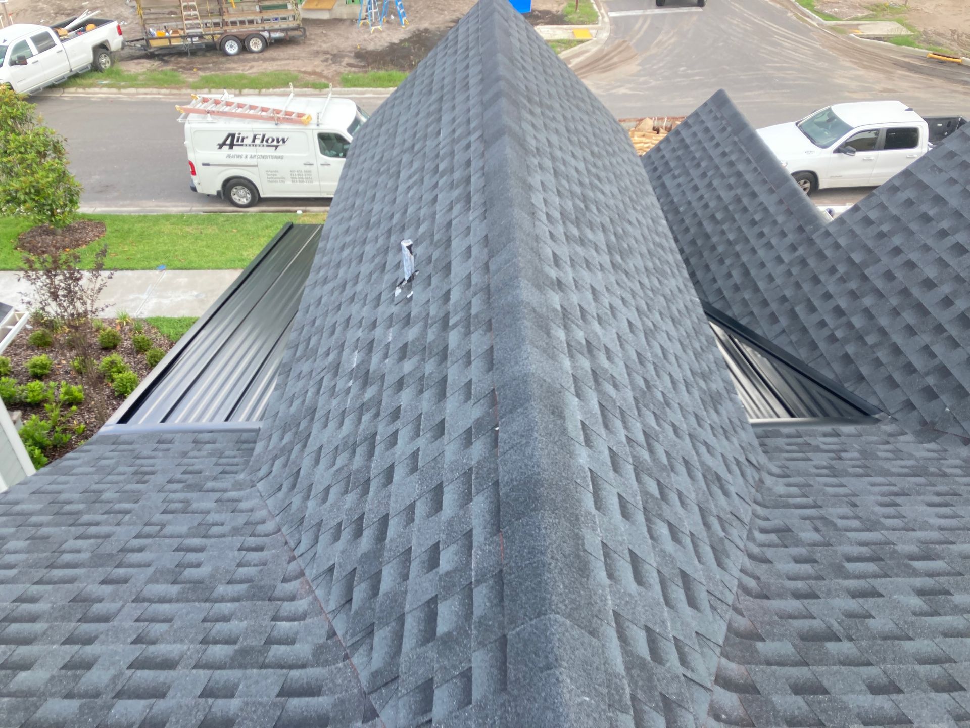 Dark gray shingle roof with steep peaks, seen from above, with a street and vehicles in the background