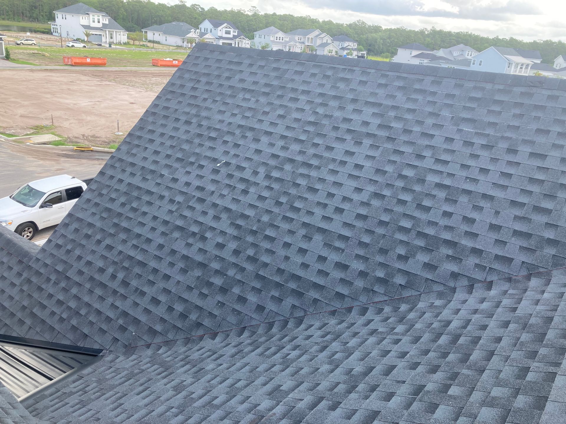 Steep shingled roof in the foreground, with a house and construction site visible in the background.