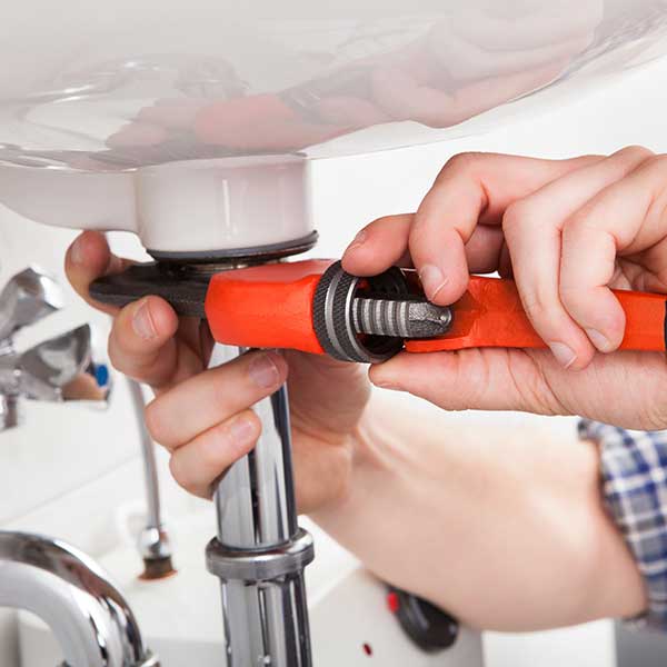 Hands tightening a bolt underneath a sink with an orange wrench