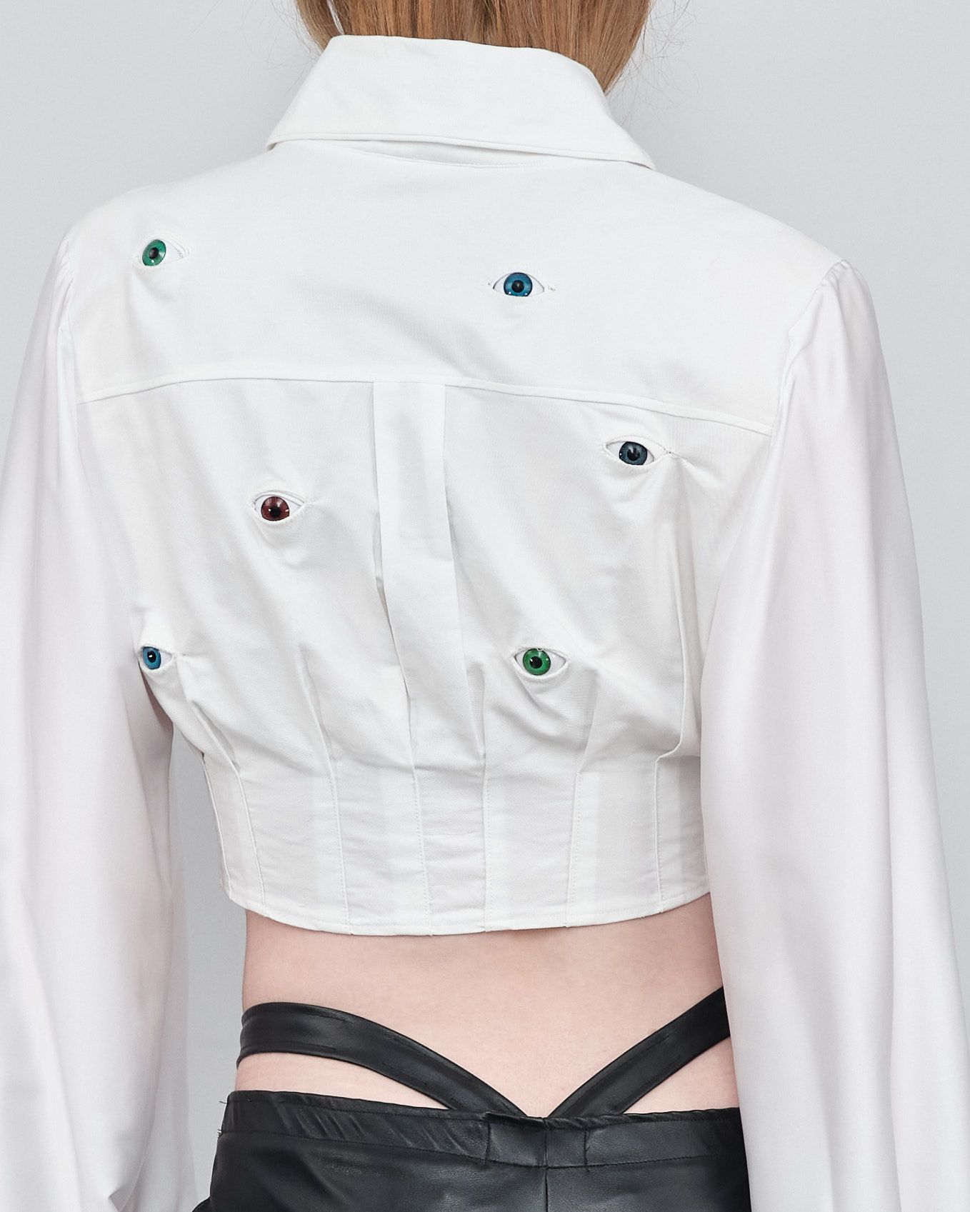 A woman is wearing a white crop top with rhinestones on the back.