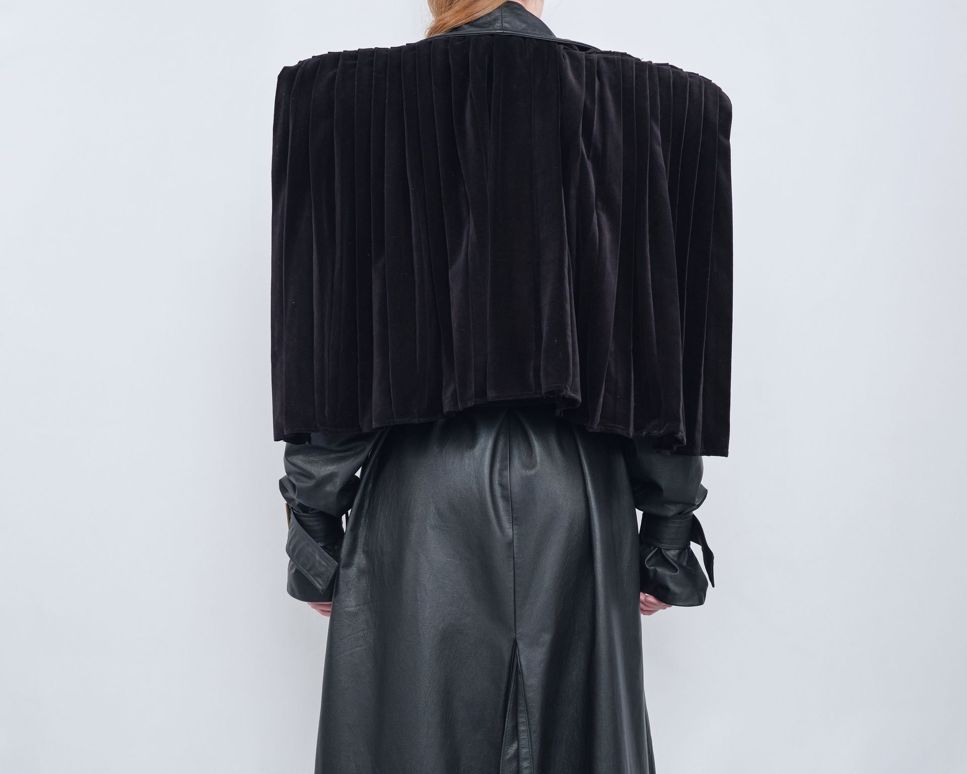 A woman is wearing a black leather coat with a black velvet cape.
