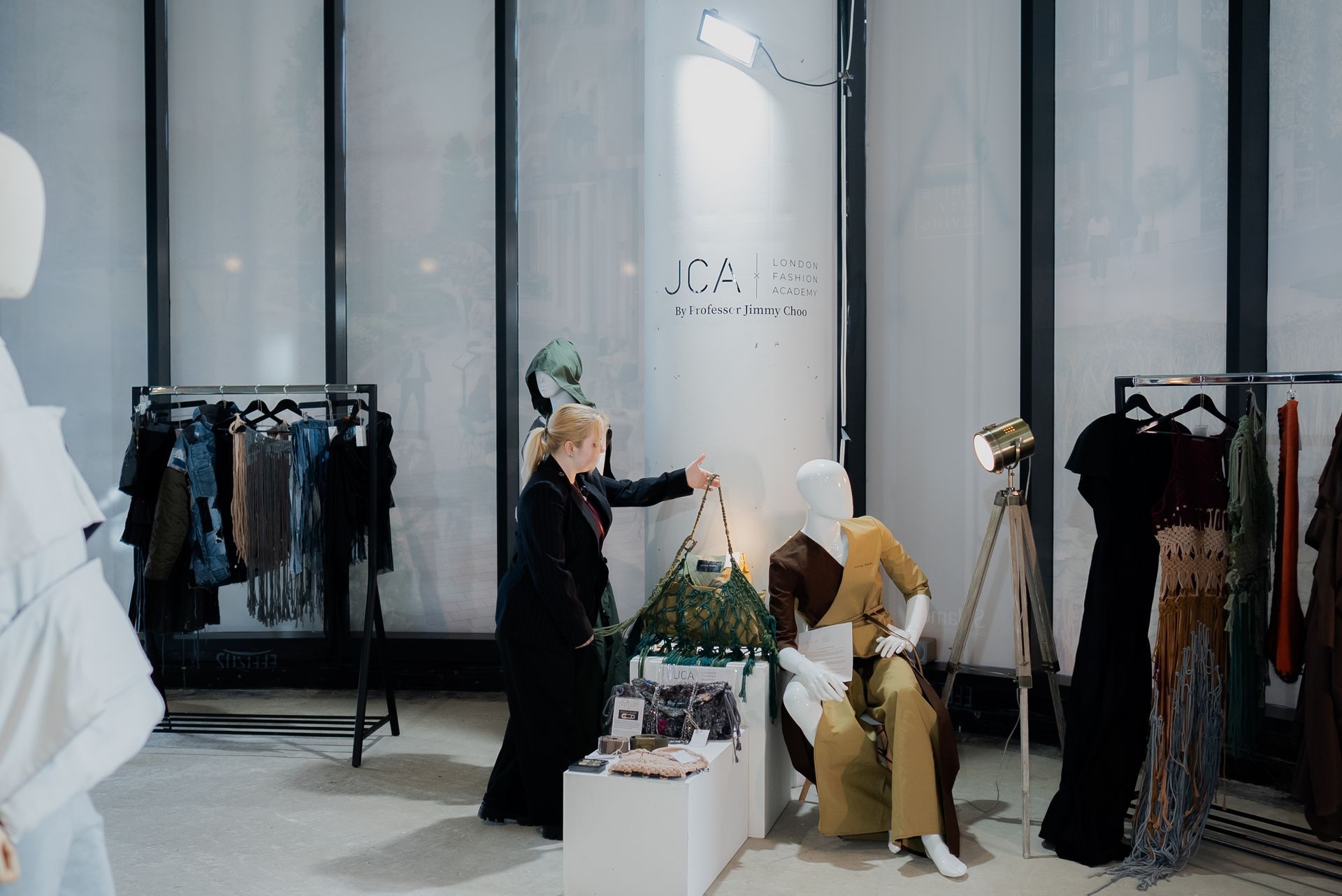 Woman arranging handbag near mannequins in a clothing store with racks of dresses.