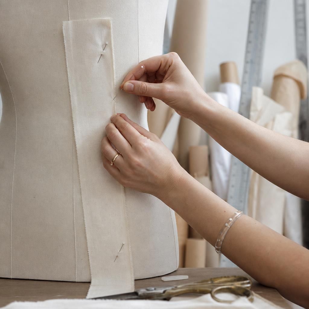 Hands pinning fabric on a dress form in a studio