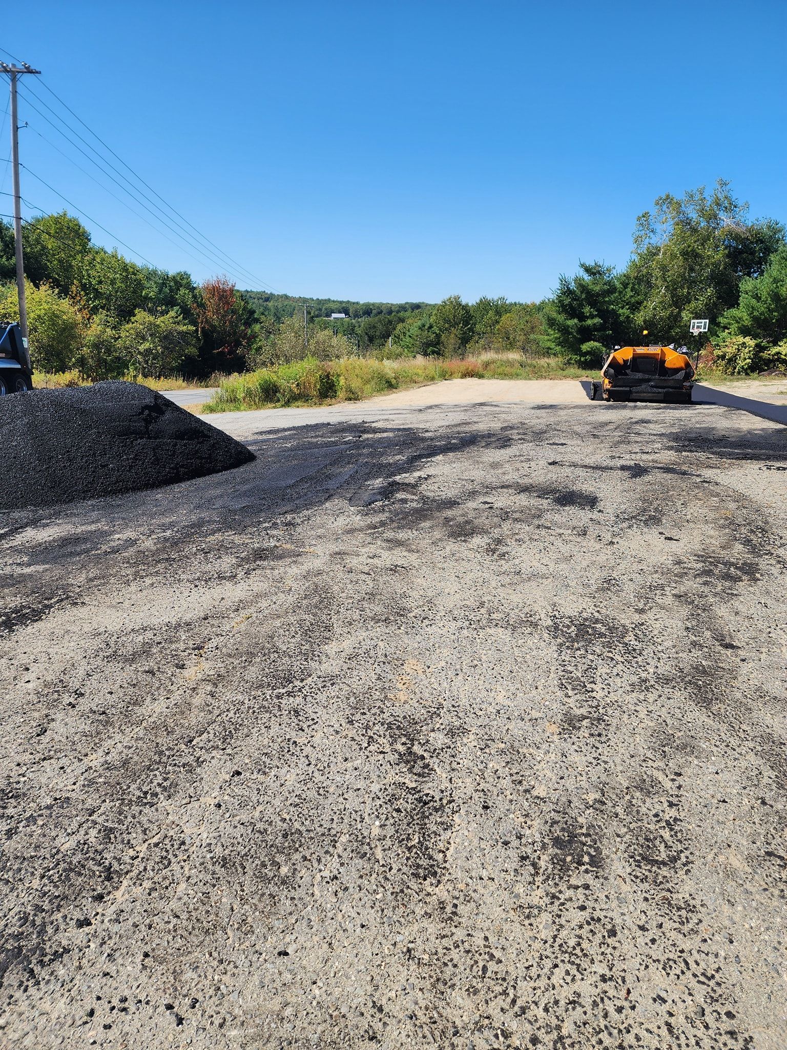 A construction site with a large pile of gravel and asphalt, featuring a parked machine under a clear blue sky.