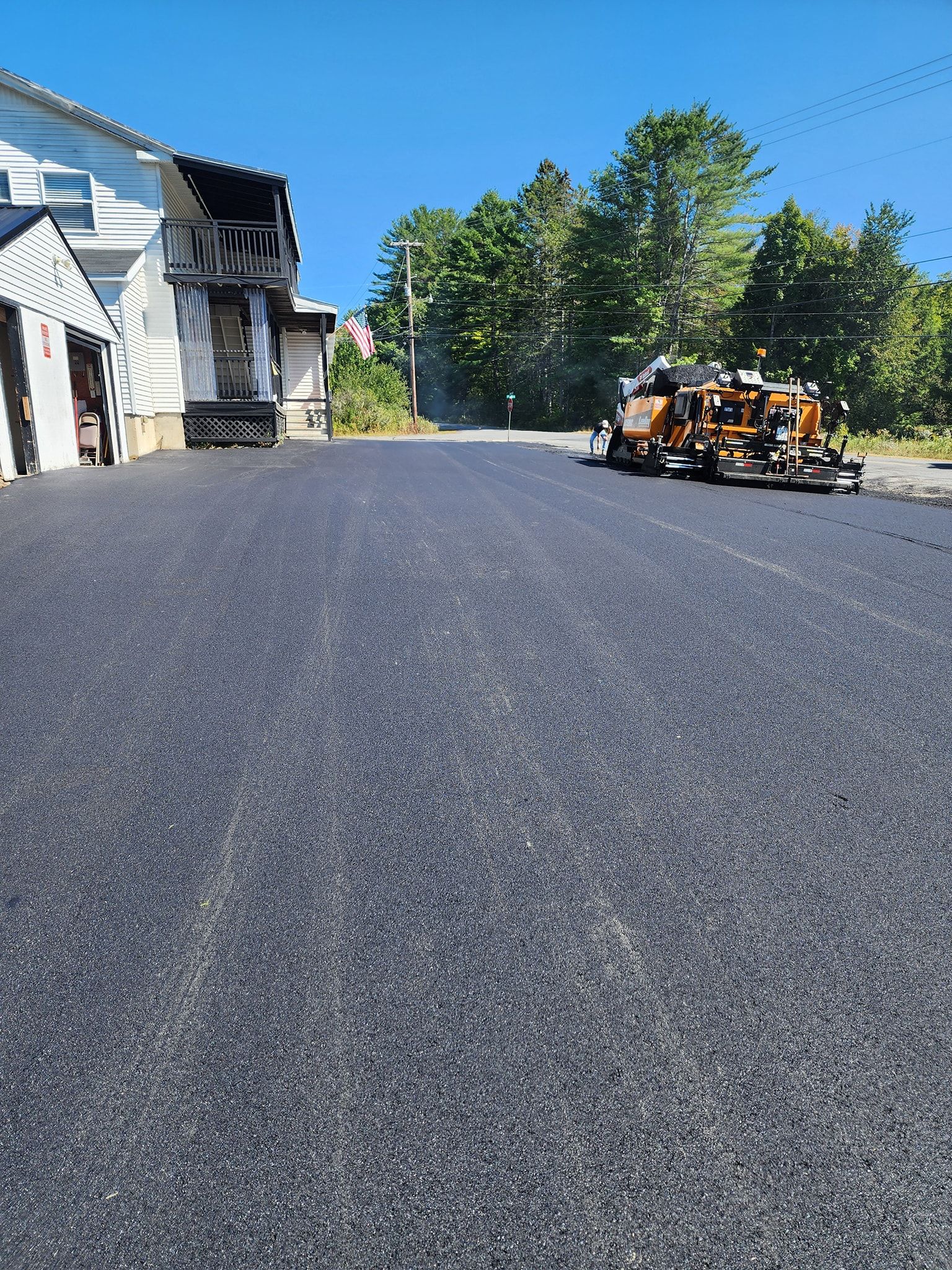 Freshly paved asphalt driveway leading to a house, with construction equipment parked in the background.
