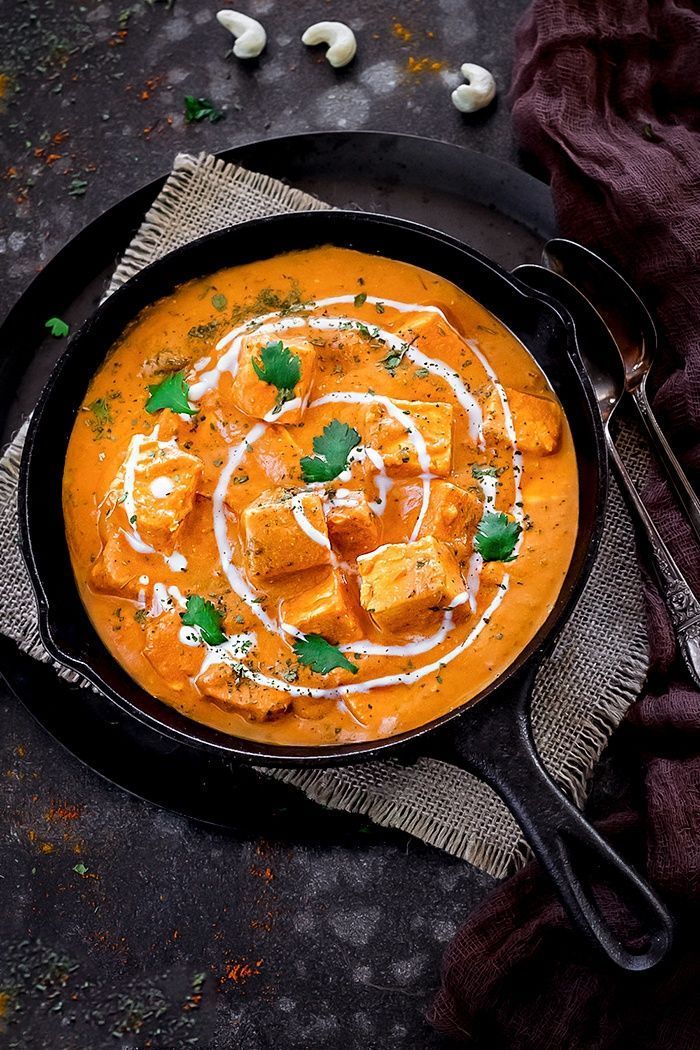 Orange curry in a black skillet, garnished with cilantro and cream swirls