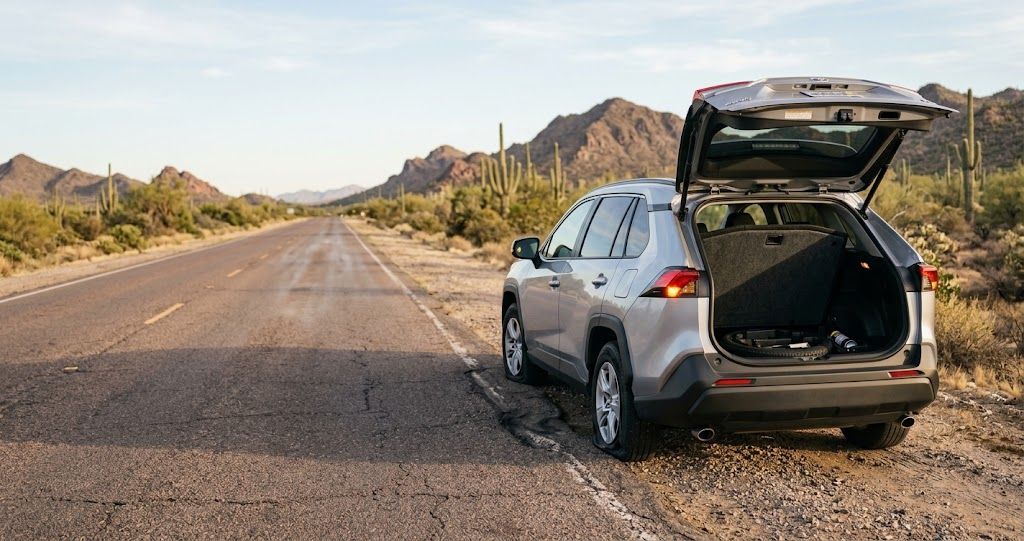 Flat front tire on an SUV stopped on a Phoenix desert highway shoulder with an empty spare tire well visible in the open trunk
