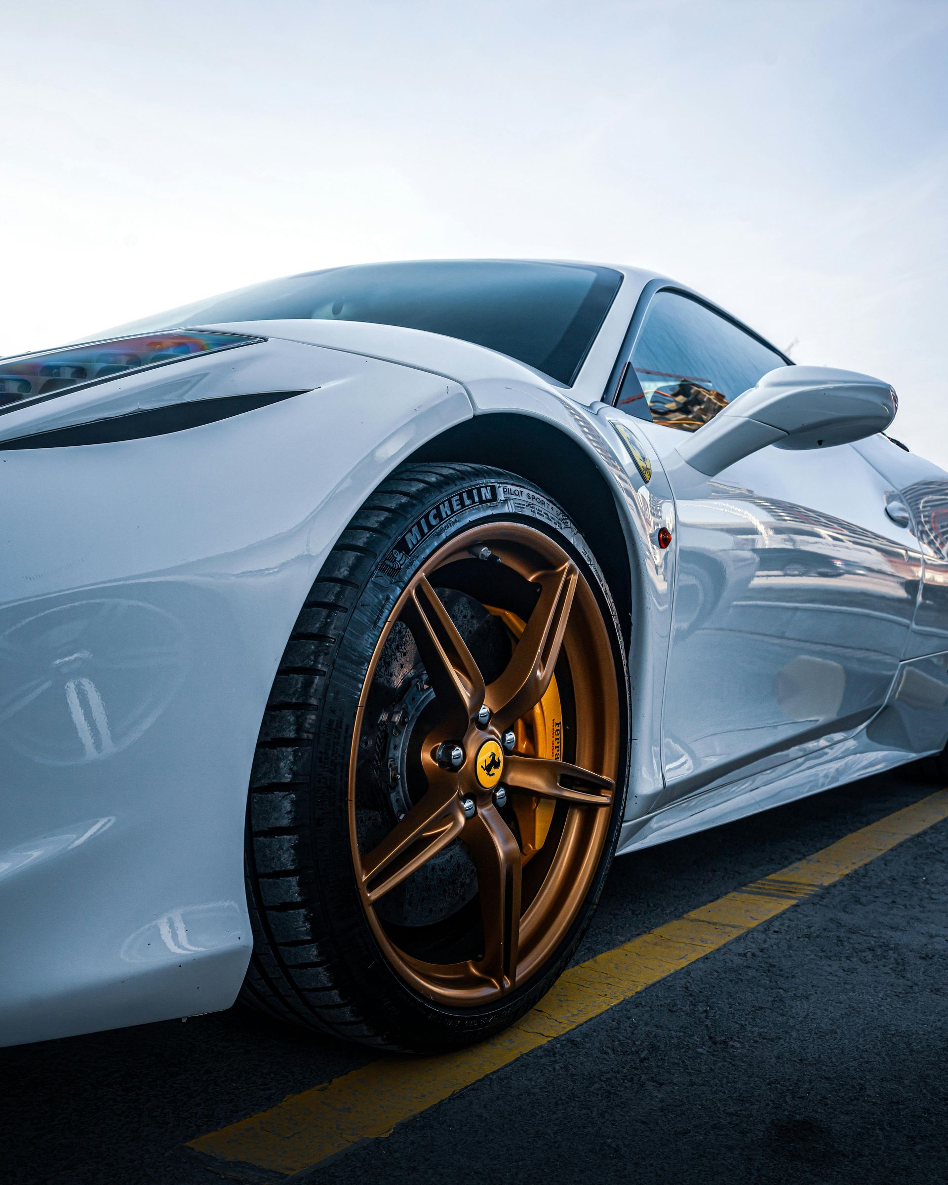 White Ferrari sports car parked, showing bronze rims and yellow brake calipers on asphalt.