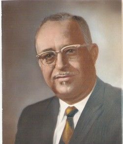 Formal portrait of a man in a suit and tie, wearing glasses, against a plain background