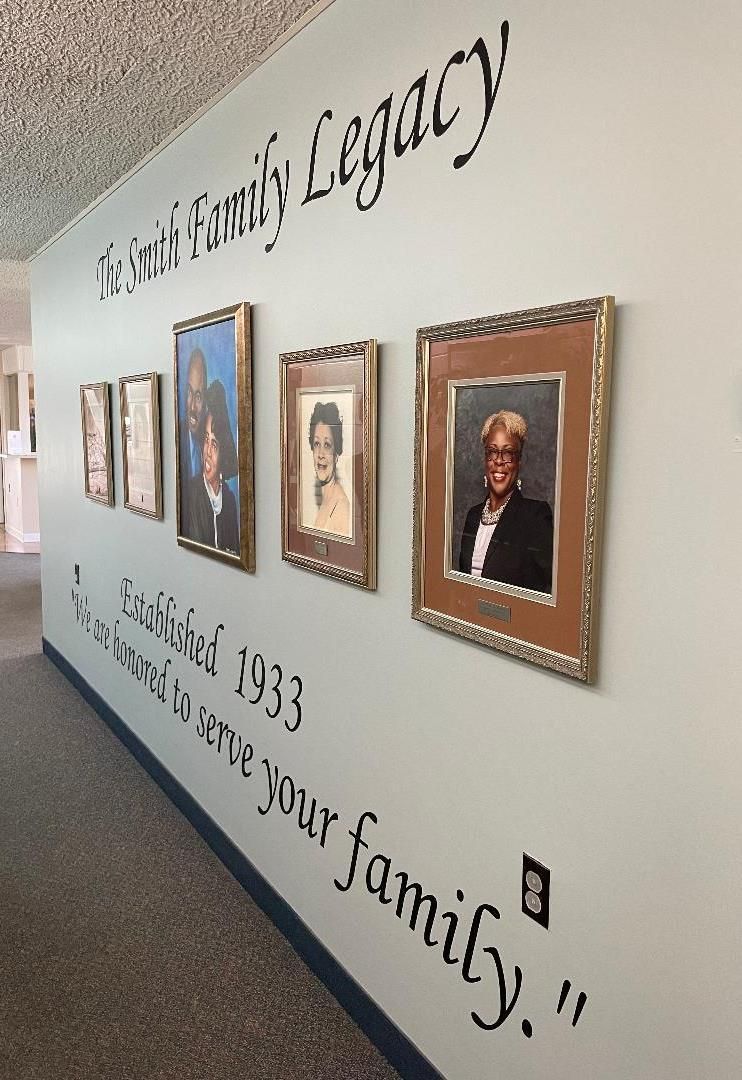 Wall with framed portraits and a large legacy quote in a hallway