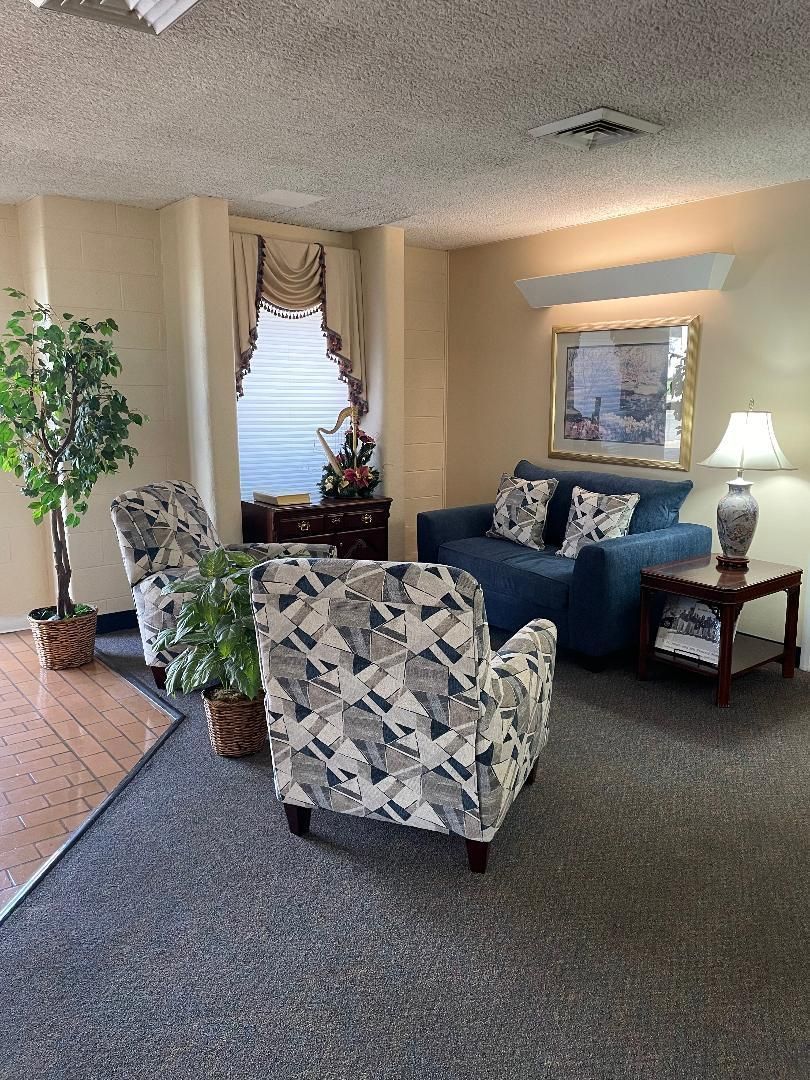 Cozy living room with floral armchair, blue sofa, lamps, plants, and a window with curtains