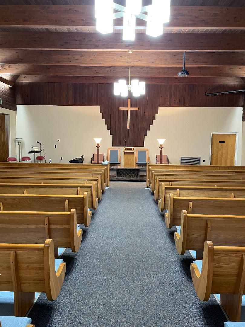 Empty church interior with wooden pews, blue carpet aisle, and altar at the front under hanging lights