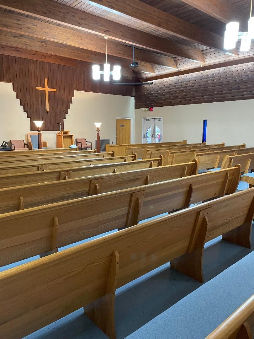 Empty church interior with wooden pews, a lit cross at the altar, and blue carpet under a vaulted wood ceiling