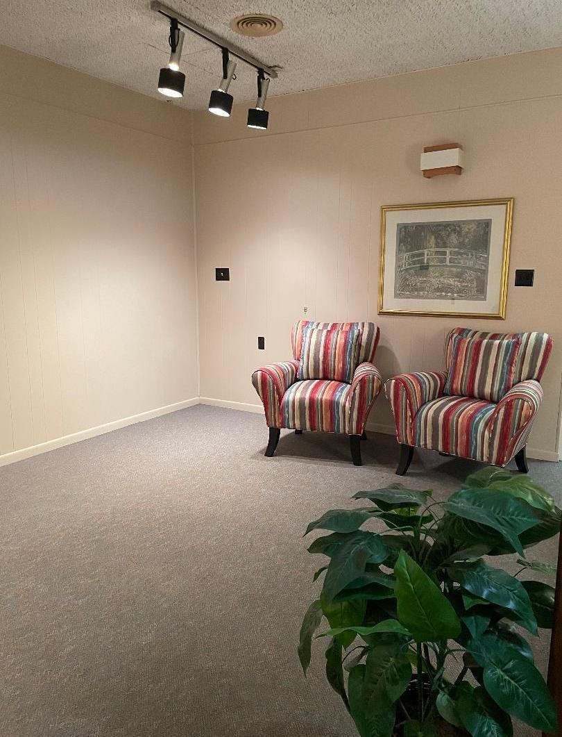 Small waiting area with two striped armchairs, framed wall art, track lights, and a potted plant.