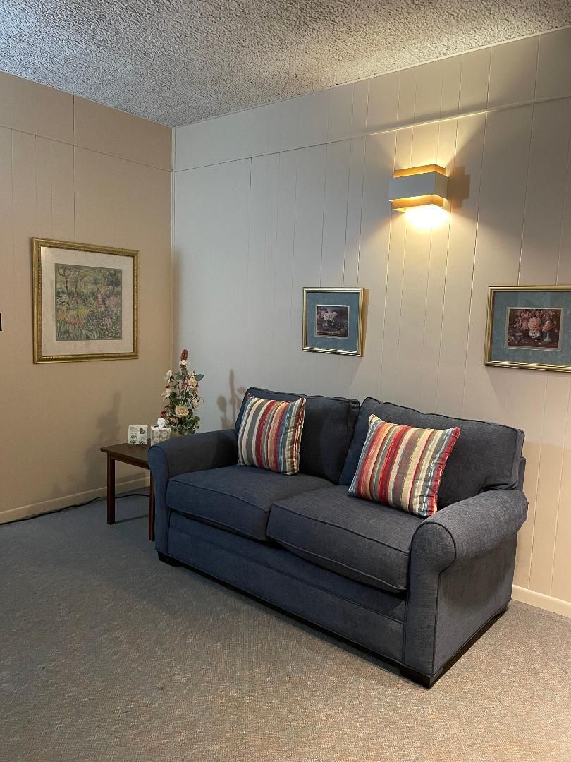 Blue couch in a beige living room with framed wall art, a side table, and wall sconce lighting