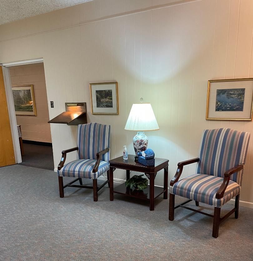 Cozy waiting room with two striped chairs, a lamp, framed art, and an open doorway.