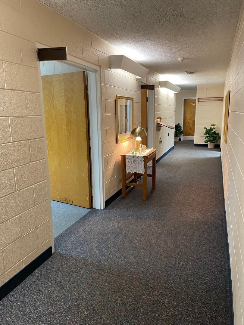 Dim hallway with doors, carpeted floor, and a small table lamp on a wooden table.