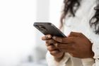 Person using a smartphone indoors, holding it with both hands against a blurred white background