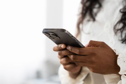 Person using a smartphone indoors, holding it with both hands against a blurred white background