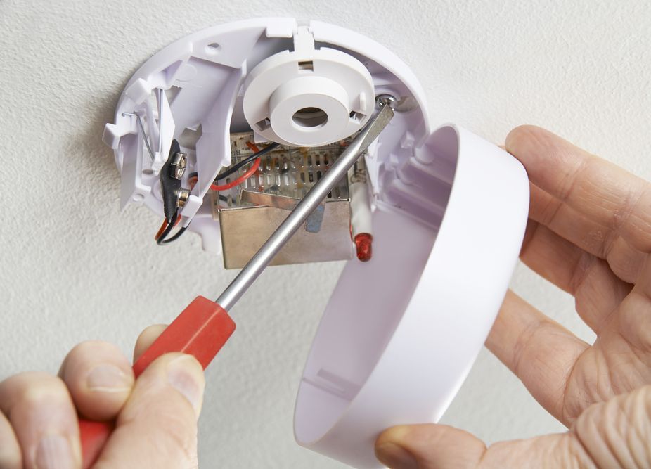 Close Up Of Technician With Screwdriver Installing Smoke Detector At Home — Alert Smoke Alarm Compliance in Maryborough, QLD