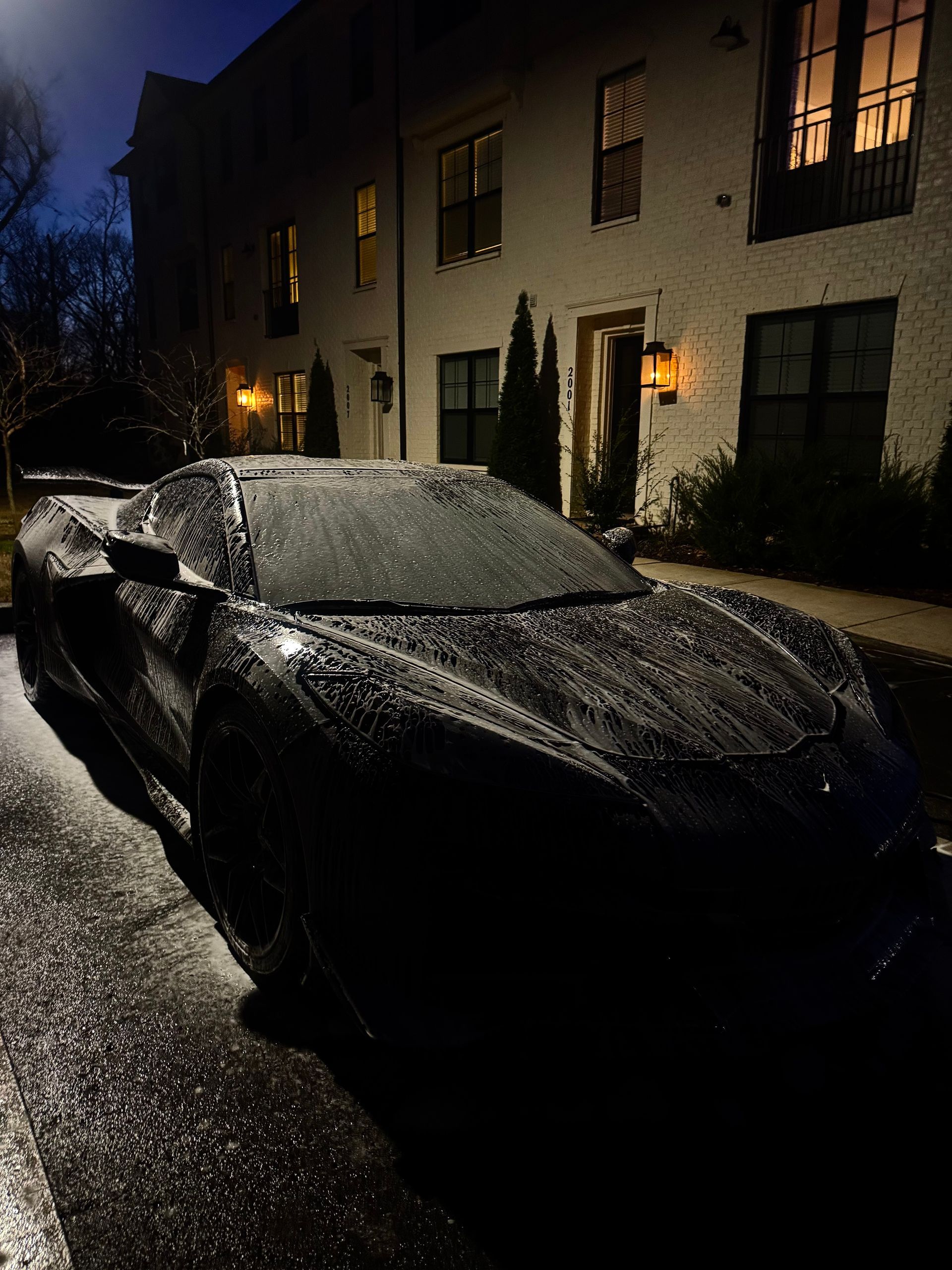 Black sports car parked on a wet street at night, with a multi-story building in the background.