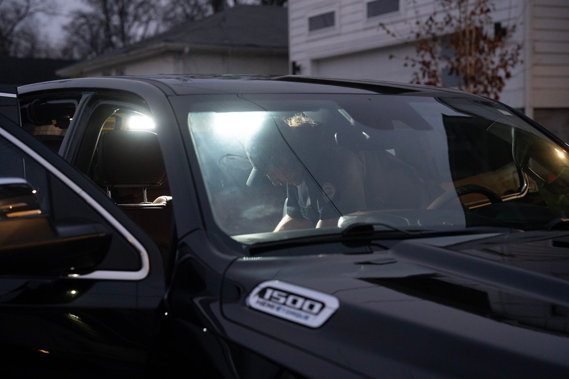 Black pickup truck with open door, bright lights illuminating interior, person inside looking down.