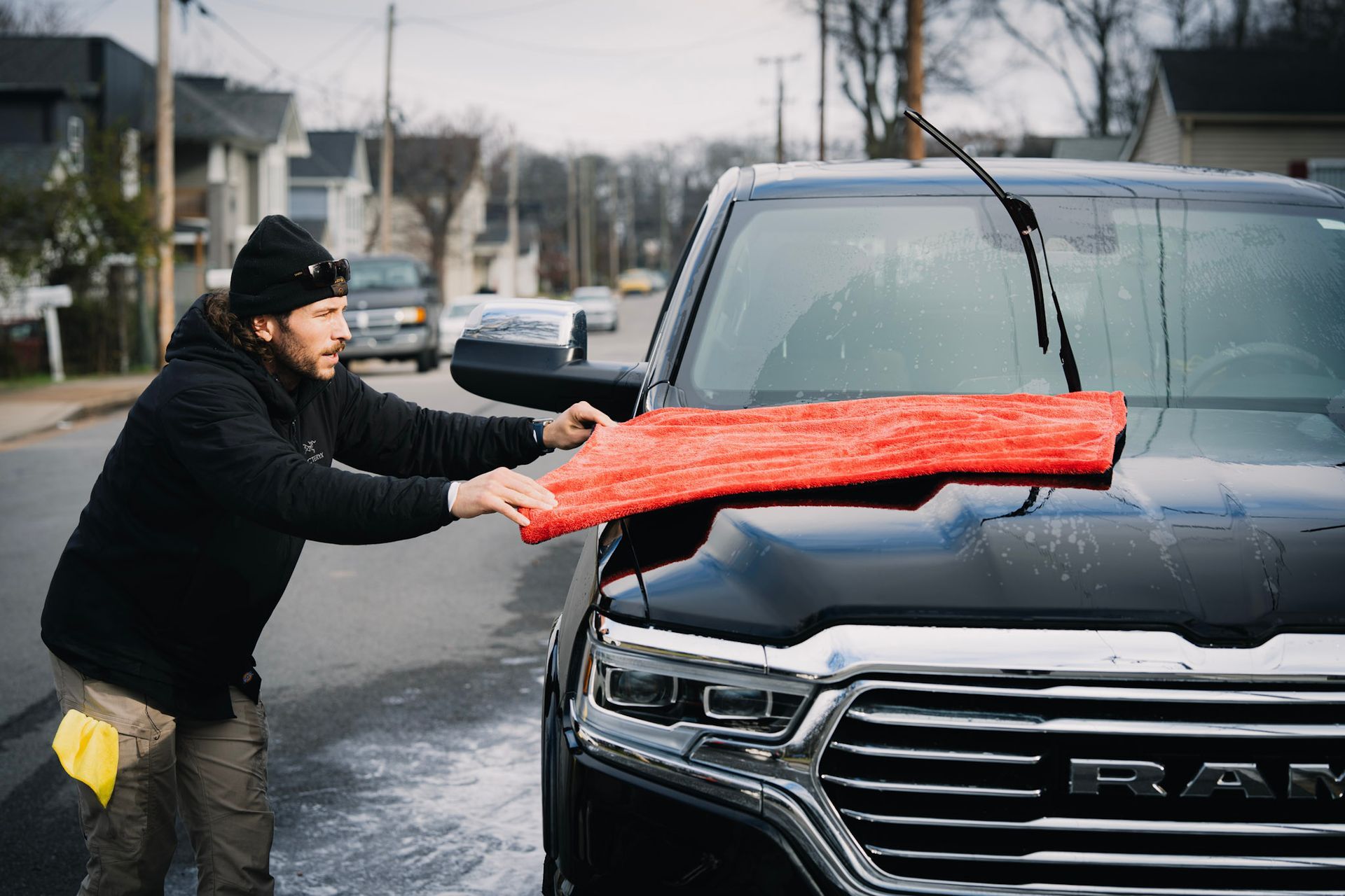 Man wiping a black truck with a red towel outdoors.