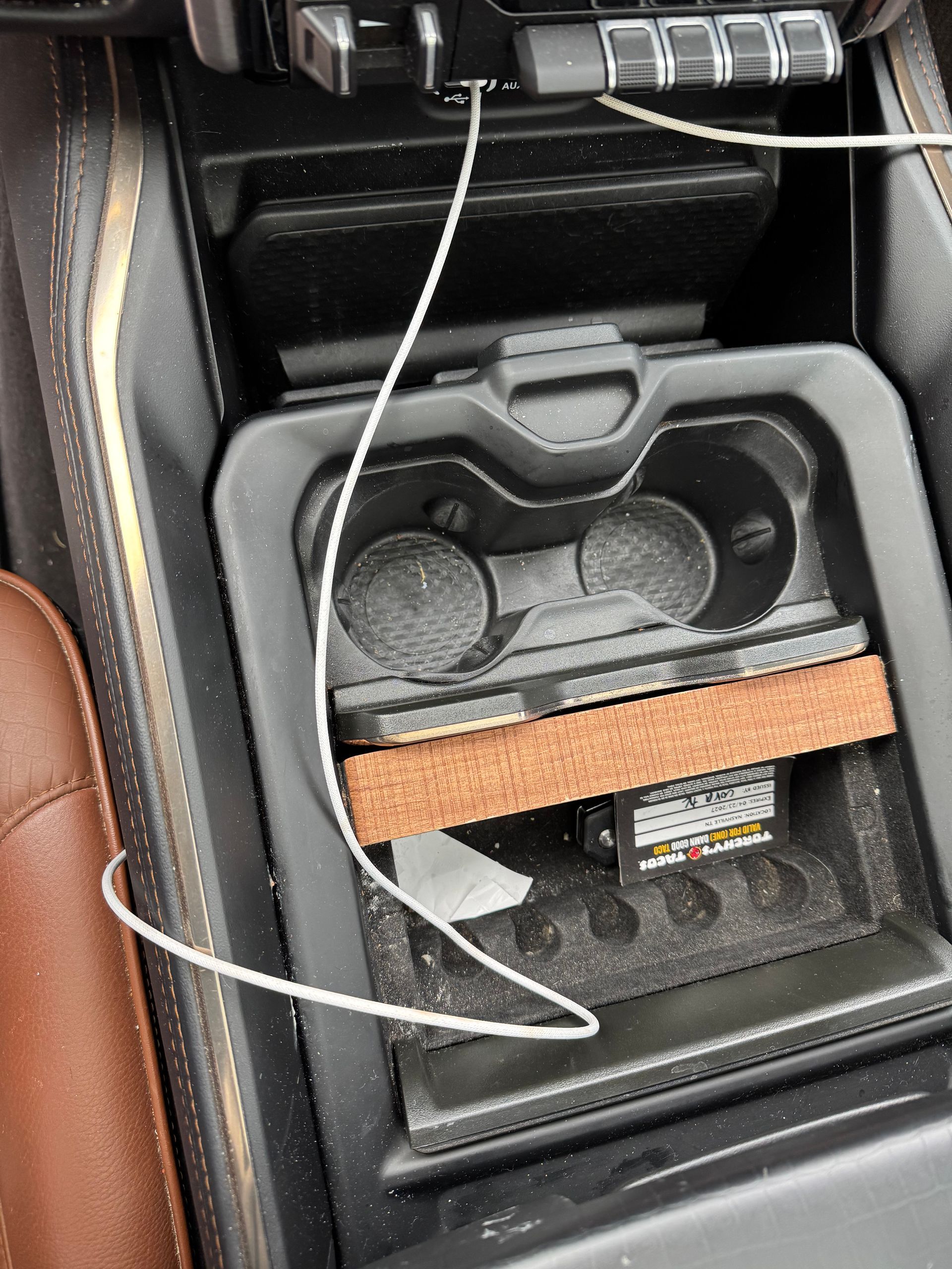 Center console of a car with two cup holders, a charging cable, and a block inside.