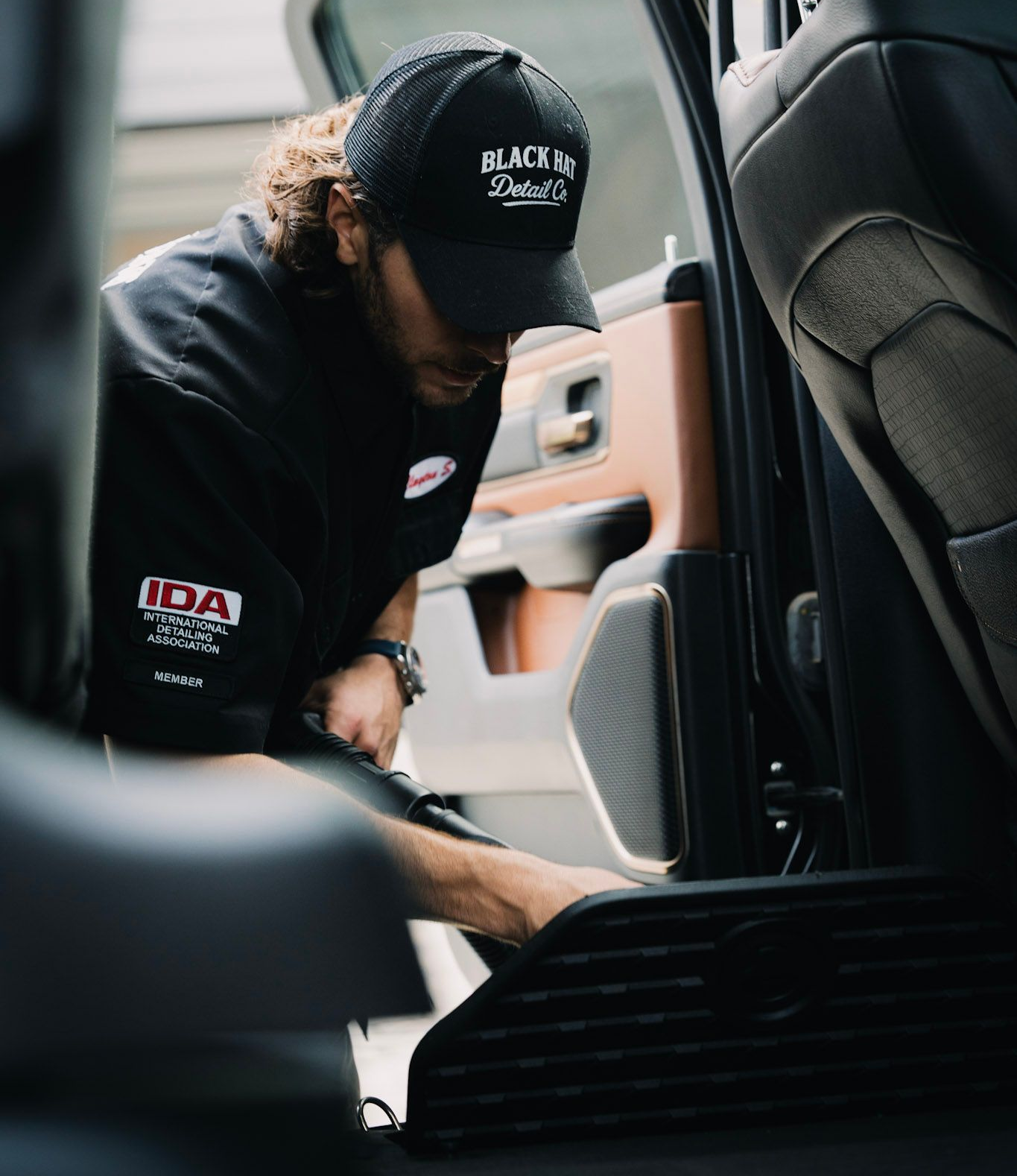 Person wearing a cap and black shirt cleaning a car's interior.