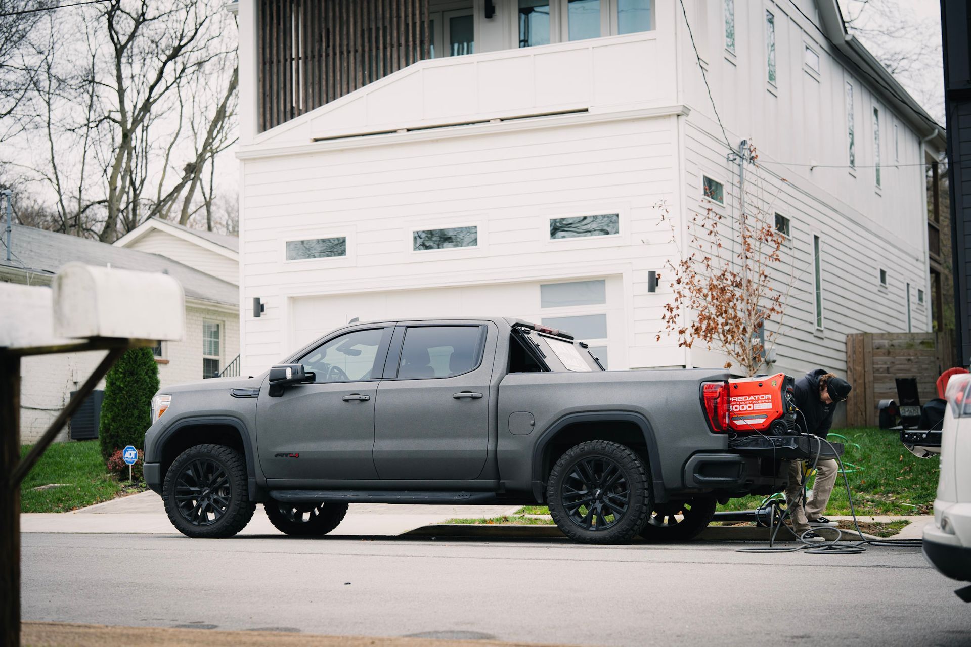 Gray pickup truck parked in front of a white house; a person is loading something into the truck bed.