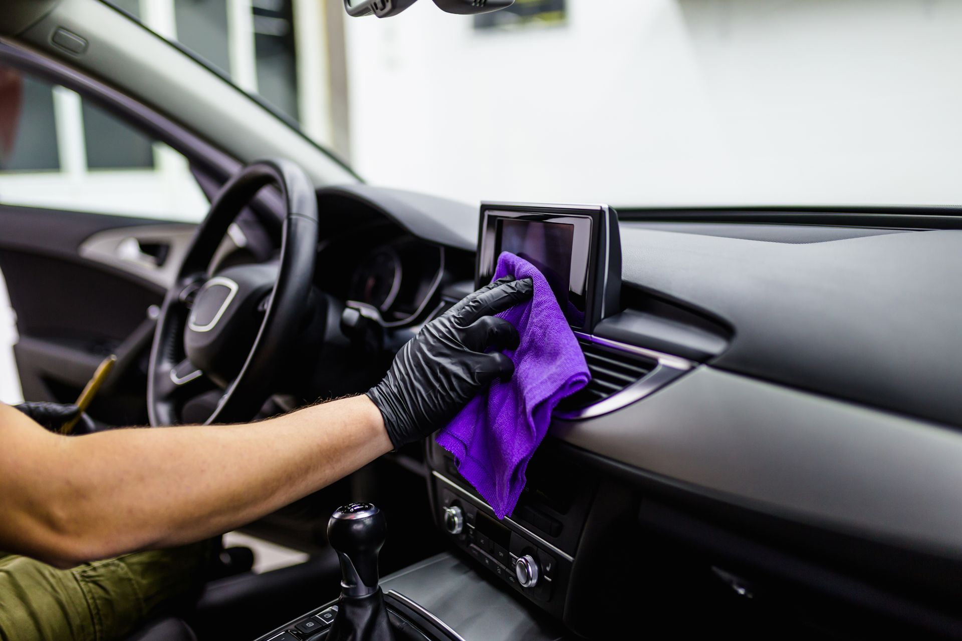 Person cleaning car dashboard with a purple cloth, wearing black gloves.