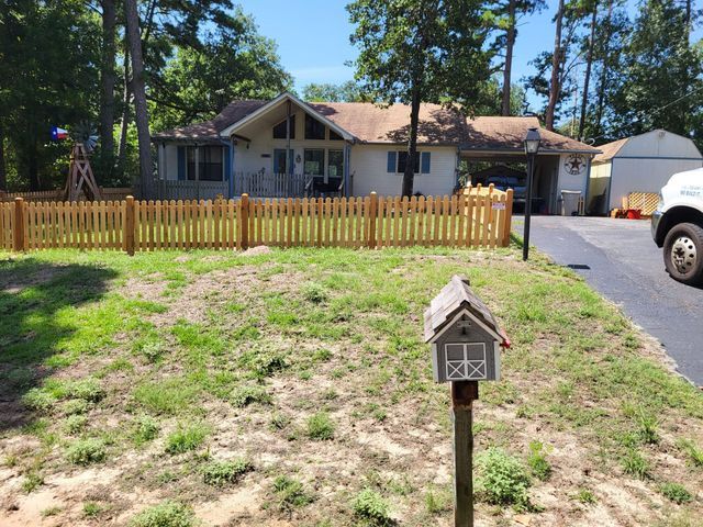 Suburban house with a wooden fence and a mailbox in front, seen across a patchy yard.